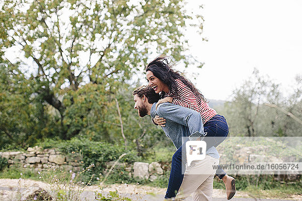 Glücklicher Mann nimmt seine Freundin beim Laufen im Freien huckepack