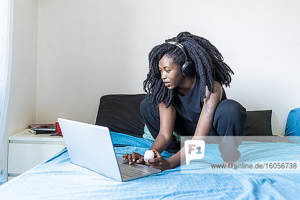 Junge Frau mit Laptop auf dem Bett zu Hause