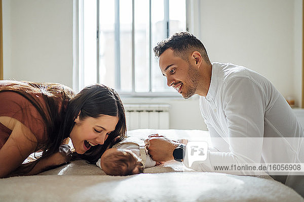 Cheerful parents playing with baby boy in bedroom at home