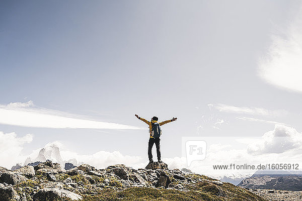 Mann mit ausgestreckten Armen auf einem Berg stehend gegen den Himmel an einem sonnigen Tag  Patagonien  Argentinien