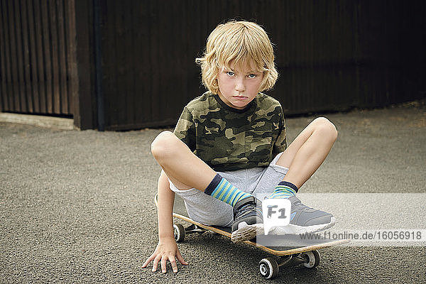 Niedlicher Junge sitzt auf einem Skateboard im Hof