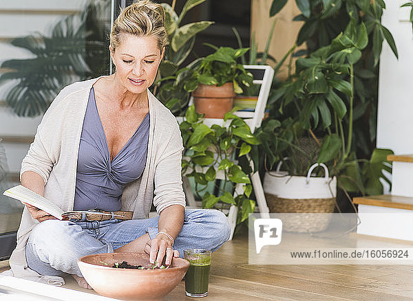 Mature woman sitting on the floor at home looking at bowl with sprouts