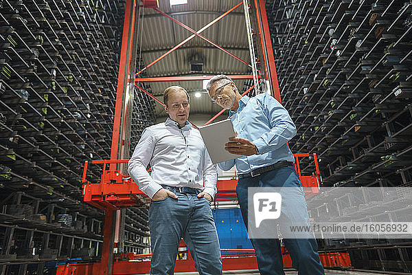 Two businessmen with tablet in a high rack warehouse of a factory