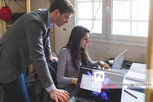 Businessman and woman sharing laptop at desk in office