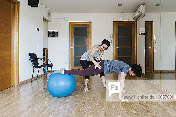 Physiotherapeutin hilft Patientin beim Balancieren auf dem Fitnessball im Fitnessstudio