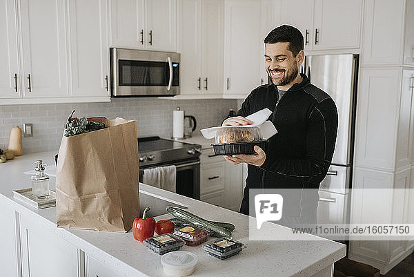Lächelnder mittelgroßer erwachsener Mann  der zu Hause in der Küche Lebensmittel aufräumt