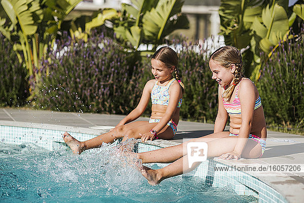 Cheerful sisters splashing water in swimming pool on sunny day