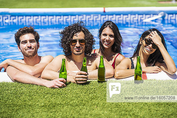 Lächelnde junge multiethnische Freunde mit Bierflaschen genießen den Sommer im Schwimmbad im Hinterhof