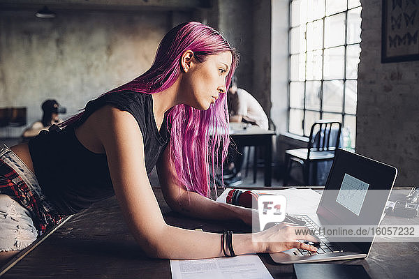 Creative businesswoman with pink hair using laptop in loft office