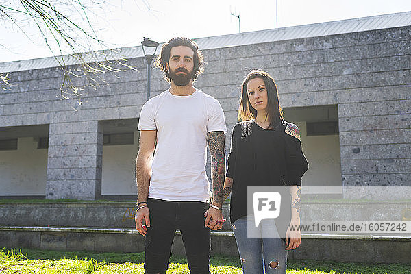 Couple holding hands while standing against building on sunny day