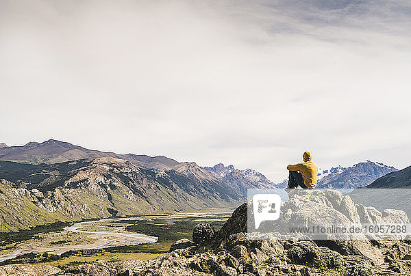 Männlicher Wanderer betrachtet die Aussicht  während er auf einem Felsen gegen den Himmel sitzt  Patagonien  Argentinien