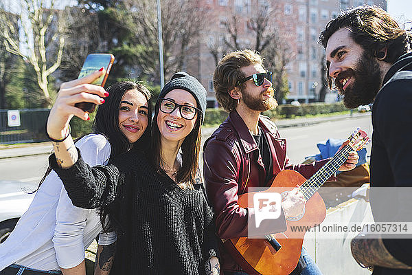 Young woman taking selfie with happy friends in city