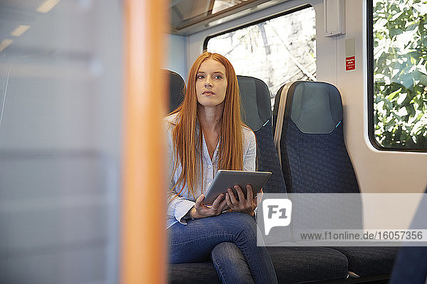 Nachdenkliche junge Frau  die ein digitales Tablet hält  während sie im Zug sitzt
