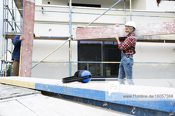 Gehörschutz auf Holz mit einem männlichen Arbeiter  der im Hintergrund Holz trägt  auf einer Baustelle