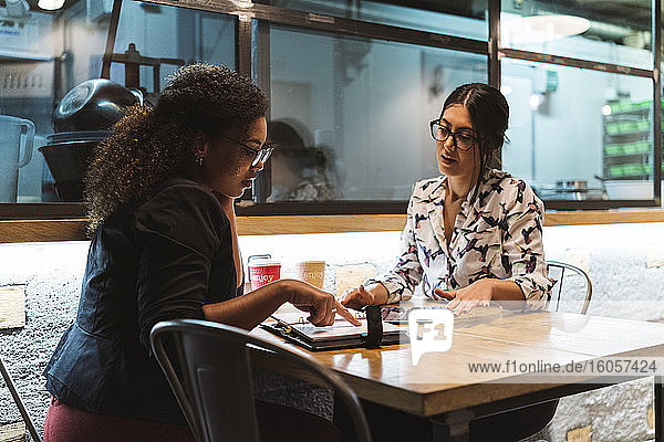 Junge Geschäftsfrau  die auf den Terminkalender zeigt  während sie mit einer Unternehmerin in einem Café plant