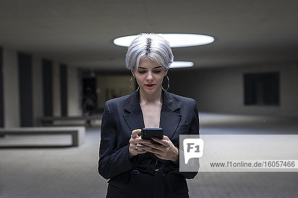 Weibliche Fachkraft im eleganten Anzug  die im Büro stehend ein Mobiltelefon benutzt