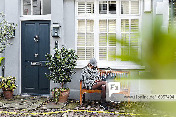 Woman writing in diary while sitting on bench on cobbled street in city