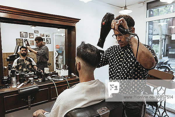 Trendy hairdresser blow drying man's hair at salon