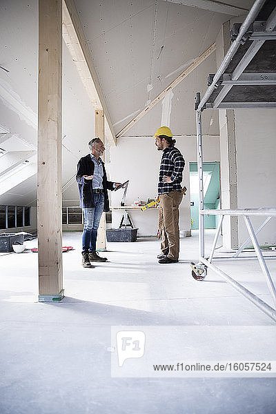 Architect and construction worker planning while standing in constructing house