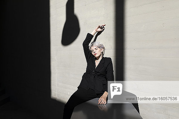 Stilvolle Geschäftsfrau in elegantem Anzug mit geschlossenen Augen sitzt auf einer Stützmauer
