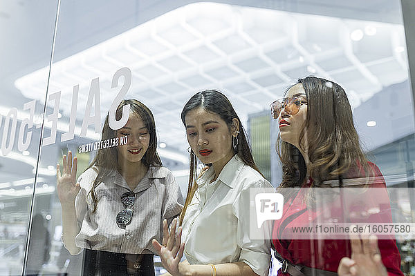 Freundinnen beim Schaufensterbummel durch Glas im Einkaufszentrum gesehen