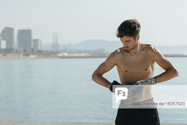 Hemdloser Boxer mit Handschuhen  der an einem sonnigen Tag am Meer steht