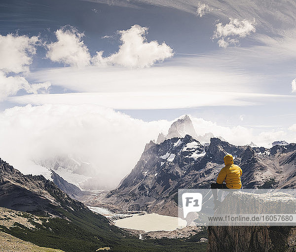 Mann schaut auf einen schneebedeckten Berg  während er auf einem Felsen gegen den Himmel sitzt  Patagonien  Argentinien