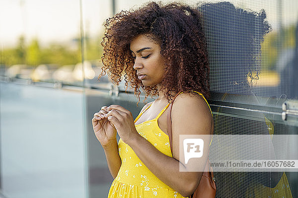 Young woman with afro hair wearing yellow dress standing by modern wall in city