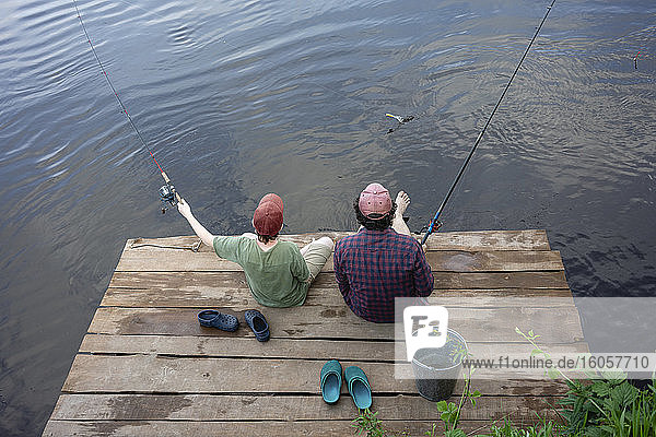 Vater und Sohn angeln im Fluss  während sie auf der Uferpromenade sitzen