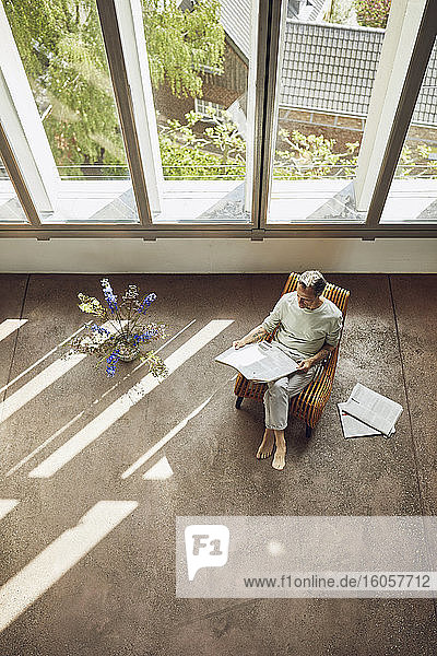 Senior man sitting on chair in a loft flat reading newspaper