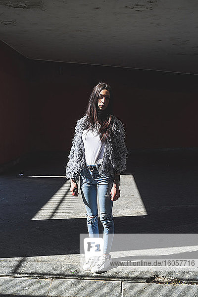Junge Frau mit Jacke  die an einem sonnigen Tag vor einem Gebäude steht