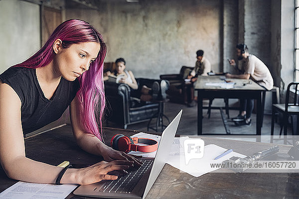 Creative businesswoman with pink hair using laptop in loft office