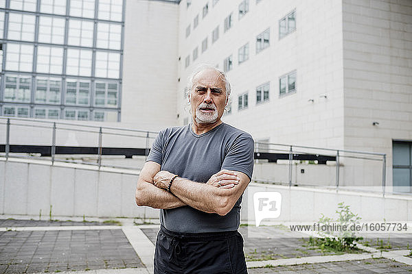 Selbstbewusster älterer Mann mit verschränkten Armen vor einem Gebäude in der Stadt stehend