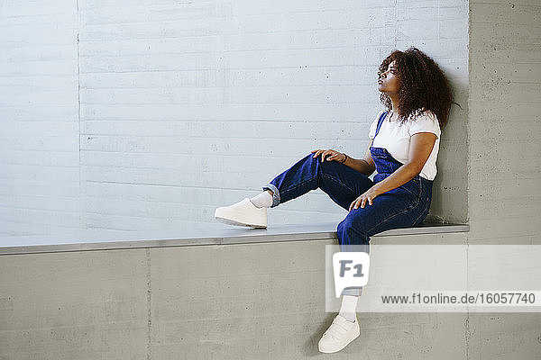 Thoughtful young woman with afro hair sitting on retaining wall