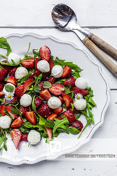 Teller mit vegetarischem Sommersalat mit Rucola  Erdbeeren  Mozzarella  Minze und Gänseblümchen