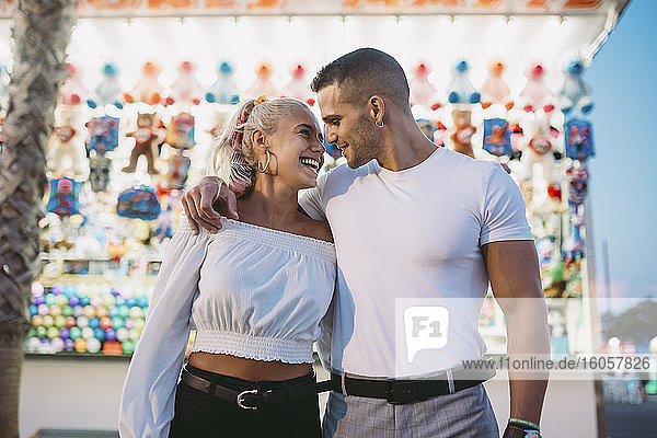 Romantischer Freund  der eine glückliche Frau ansieht  während er in einem Vergnügungspark an einem Verkaufsstand steht
