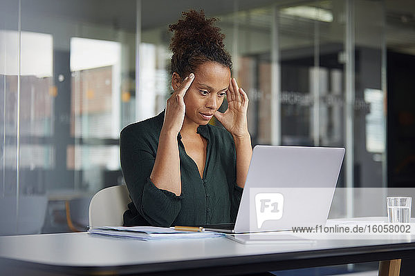 Porträt einer nachdenklichen Geschäftsfrau am Schreibtisch mit Blick auf einen Laptop