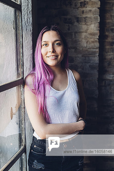 Porträt einer lächelnden jungen Frau mit rosa Haaren im Loft
