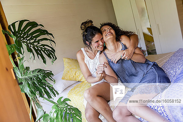 Fröhliche Frau  die ihre Freundin umarmt  während sie auf einem Bett in einem Landhaus sitzt