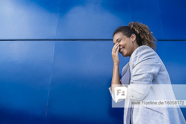 Lachende Geschäftsfrau vor blauer Wand