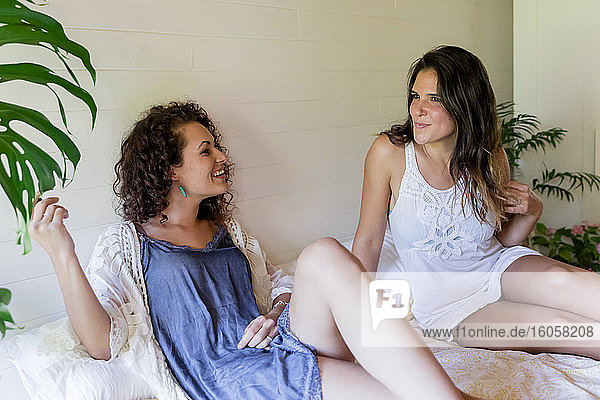 Glückliche junge Freundinnen unterhalten sich auf einem Bett in einem Ferienhaus