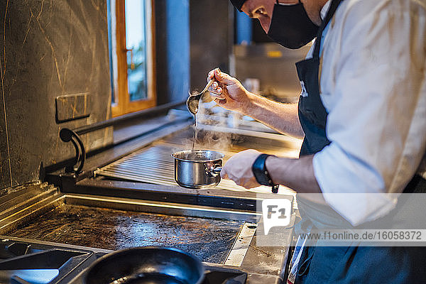 Koch mit Schutzmaske bei der Zubereitung einer Soße in einer Restaurantküche