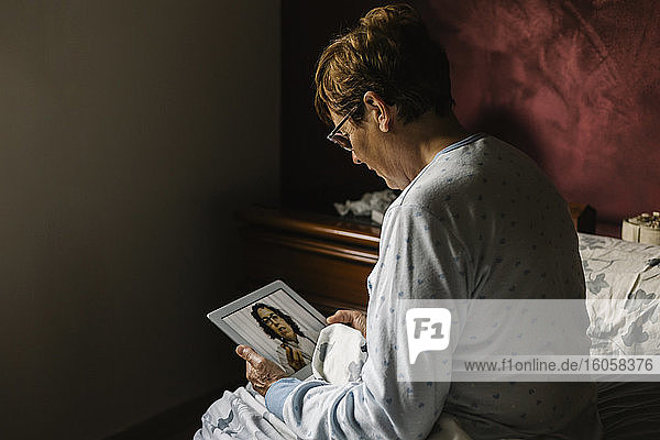 Ältere Frau im Schlafzimmer bespricht sich per Videoanruf mit einem Arzt zu Hause