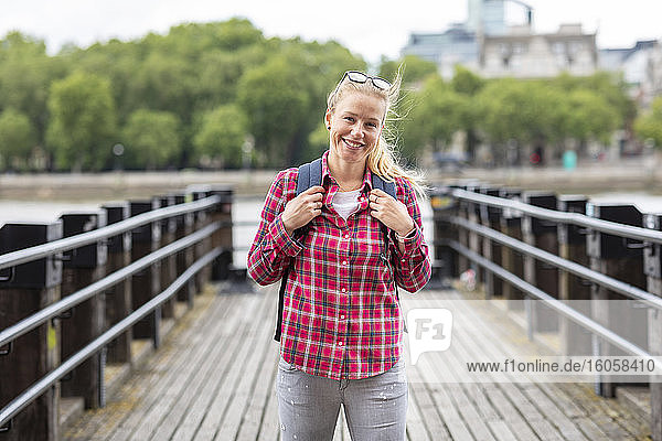Lächelnde Frau im mittleren Erwachsenenalter mit kariertem Hemd auf einer Brücke in der Stadt stehend