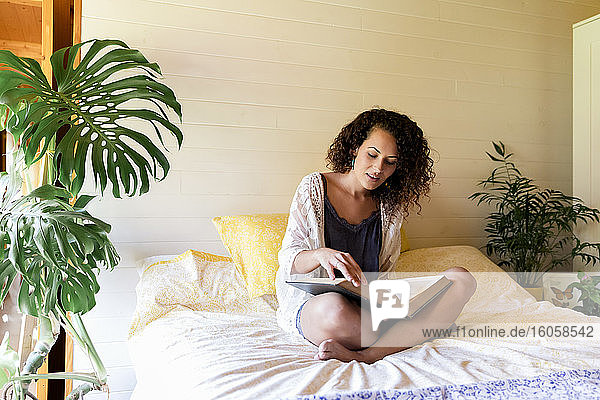 Junge Frau liest ein Buch  während sie auf einem Bett in einer Blockhütte sitzt