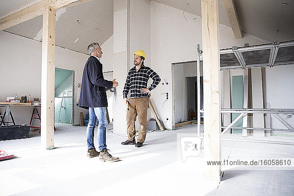 Architect and construction worker discussing while standing in renovating house