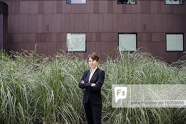 Confident businesswoman with arms crossed standing by plants in city