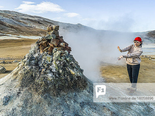 Eine Touristin steht am Rand einer Fumarole  um den Dampf zu spüren. Dieser geothermische Ort ist bekannt für seine blubbernden Schlammtümpel und dampfenden Fumarolen  die schwefelhaltiges Gas ausstoßen; Skutustadahreppur  Nordost-Region  Island