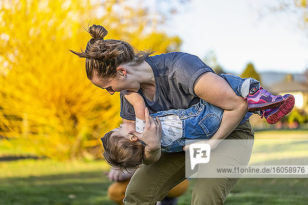 A mother plays with her toddler daughter in a park with autumn colours; North Vancouver  British Columbia  Canada