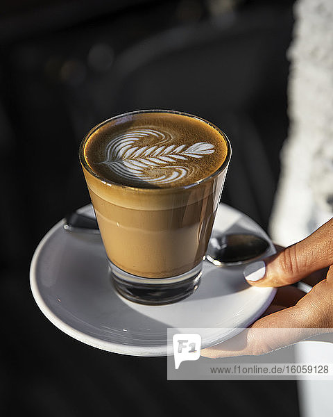 Cafe Latte mit Kaffee-Kunstdesign  das von einer Frau in der Hand gehalten wird; Melbourne  Victoria  Australien